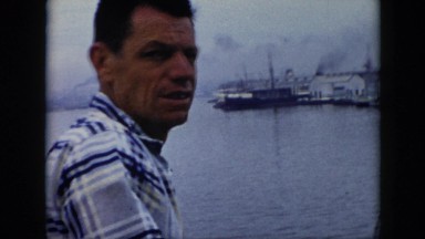 1956: a couple standing on the shore of a lake with many buildings CUBA