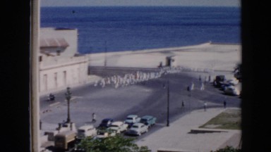 1956: sea people troops cars parked street lamps road trees around CUBA