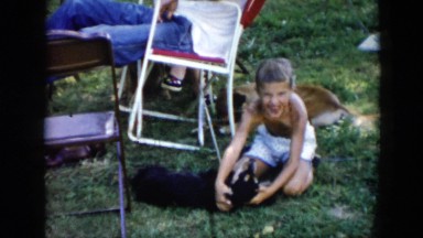 1956: girl on grass playing with holding puppy near person rocking in red chair