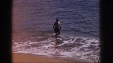 1961: Male Swimmer Emerging from Waves and Running onto Wet Sand Shore