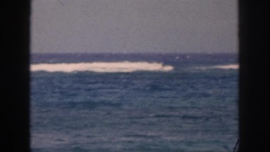 1961: totally beach seen looking blue water surfing waves, little bit of wind.