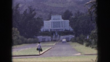 1961: woman with bags waiting on a curb in front of stately white building