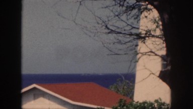 1961: white house with red roof near trees and a blue ocean in the background