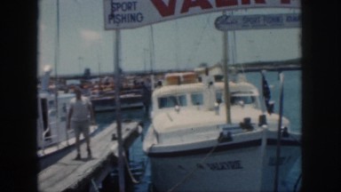 1961: a sport fishing vessel for charter is tied to a dock in a small harbor