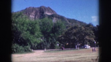 1961: the cars driving on a road in front of a hill. HAWAII