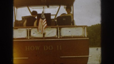 1961: ship sailing water people sitting inside flag waving trees around