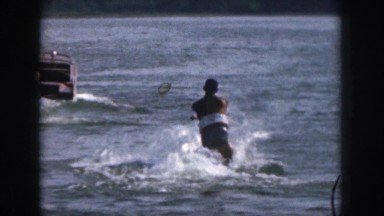 1961: man on water skis pulled by motor boat on lake surrounded by trees