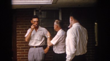 1958: four gentlemen in business attire stand outside a brick building, smoking