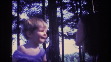 1975: blonde toddler with food gives a kiss to a woman with long hair
