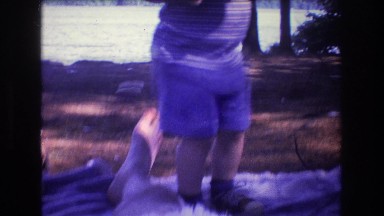 1975: toddler plays on blanket near lake. BAXTER MAINE