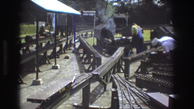 1975: a maze of miniature train tracks on trestles with workers crossing back