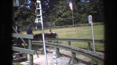 1975: two men and a baby riding a miniature train along a train track BAXTER
