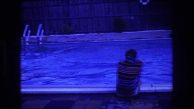 1975: a man is squatting on the bank of a swimming pool BOSTON