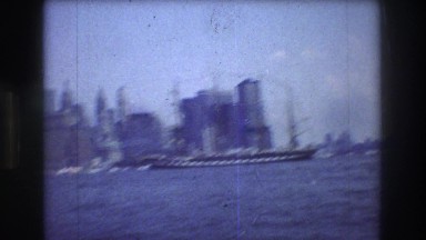 1976: large vessel sailing through the water with an urban setting backdrop