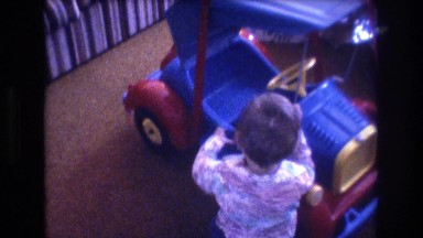 1975: a happy boy playing with a toy car while a dog and an adult watching over