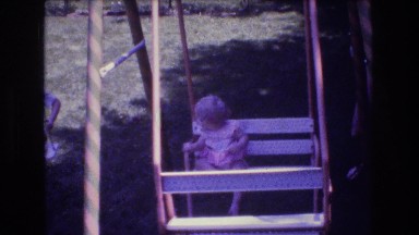 1976: swingset with little children swinging in a glider seat and on a swing