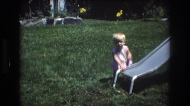 1976: nearby a slide baby in a grassy garden falling down as dog pass by