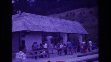 1976: people standing alongside road in a house rocky terrain trees around
