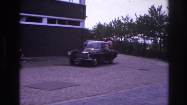 1967: a small car driving past the front of a building with people PARIS FRANCE