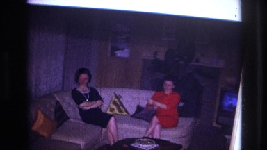 1967: Women Sitting on Couch in Living Room Man Standing Between Ladies