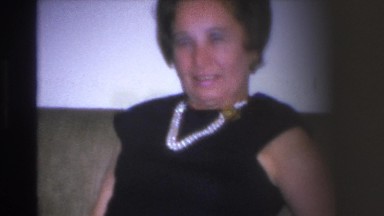 1966: Older Woman Sits on Sofa Wearing Black Dress and Pearls in Hoboken, NJ