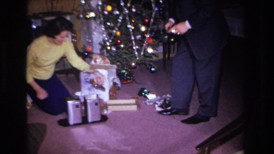 1966: a woman on her knees in the living room opens christmas presents