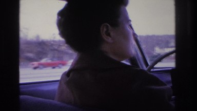 1966: woman driving looking back cars passing highway houses trees street lamps