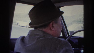 1966: man driving on road talking wearing hat speed cars moving by