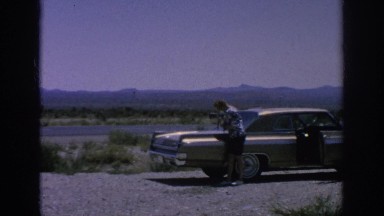 1962: a woman walks her poodle on the trunk of her car in the middle of nowhere