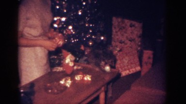 1962: woman holding bows kneels by christmas tree and plays game with dog
