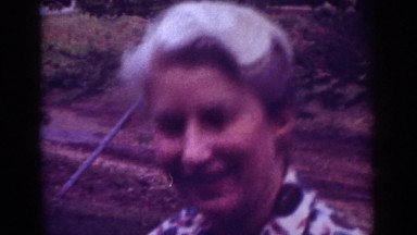 1962: vintage video of an older woman sitting outside with her leashed poodle.
