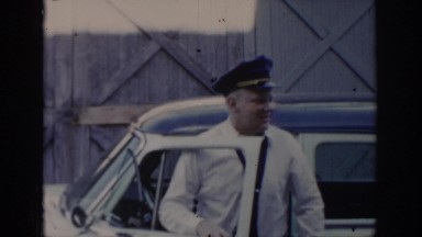 1965: two men, one of them with a cap, talking next to a vehicle