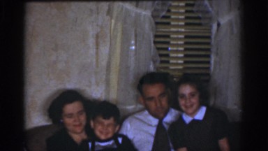 1968: children sitting on parents laps on love seat watching evening television