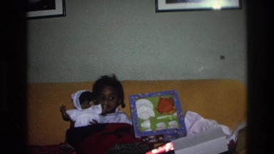 1975: a small child sits under a blanket and plays with a doll next to a box