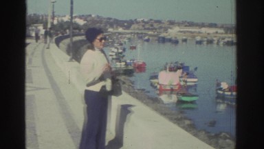 1976: A Lady Standing by a Pier Filled with Boats GREECE