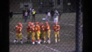 1975: urban youth football team viewed behind chain linked fence BRONX NEW YORK