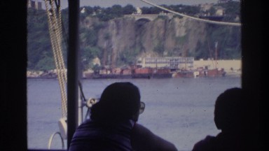 1975: people on boat look out at water that is rapidly flowing with a bridge