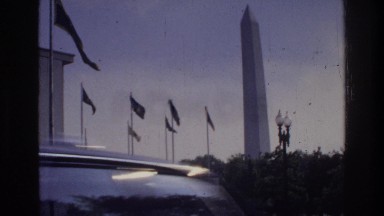 1975: a tall memorial with flags and trees that has cars driving past it