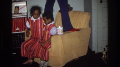 1975: adult stands on upholstered-chair arms to hang cards