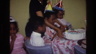 1976: mother helping child cut birthday cake surrounded by other children HARLEM