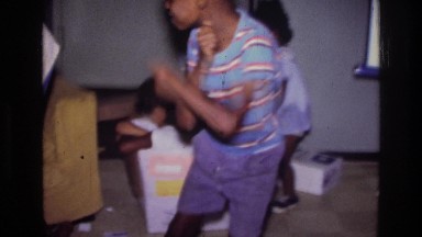 1976: a family is moving and a boy in the foreground is grooving