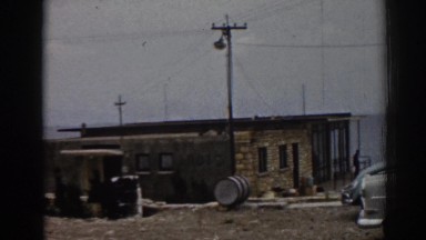 1962: coastal building near large body of water, man standing on porch EPHESUS