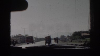 1962: driving slowly down a road past a van, people on the side of the road