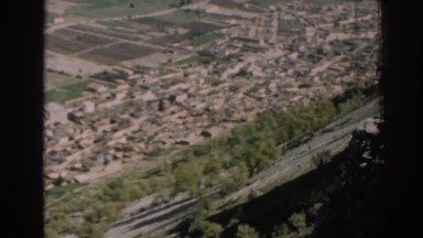 1962: a built-up area lies at the base of a tree studded steep mountain slope