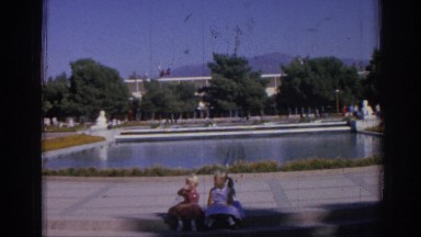 1962: twin girls sitting on a bench in a garden like place with water IZMIR