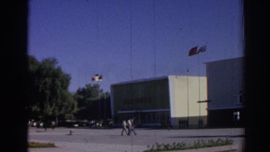 1962: pedestrians walk past a building flying foreign flags on a windy day IZMIR