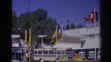 1962: a multi-story building flies many turkish flags and has buses parked