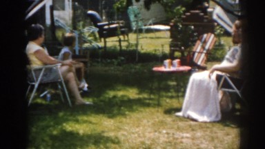 1963: family gathered around outside sitting in chairs talking to one another