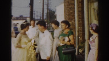 1963: bride and other wedding-goers interact with one another outdoors