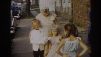 1963: a young boy and girl dressed in formal clothes pose on the sidewalk